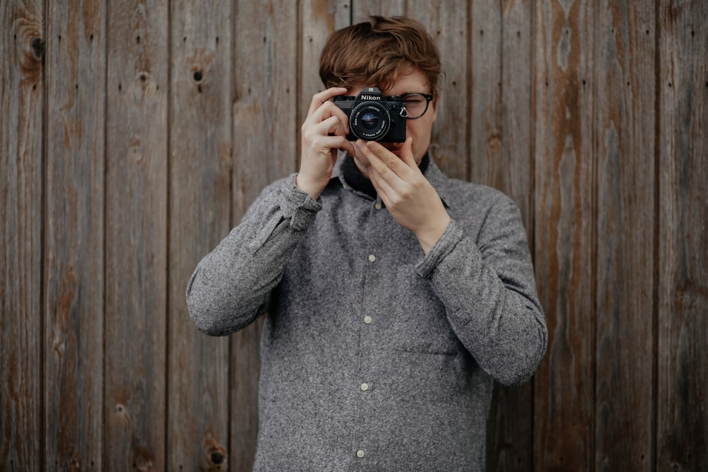 검은 다리 카메라를 들고 사진을 찍고 갈색 나무 벽 근처에 서 있는 남자