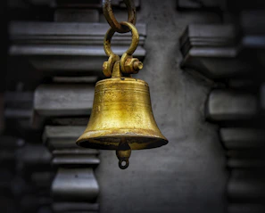 A golden temple bell hanging gracefully against a deep maroon backdrop.