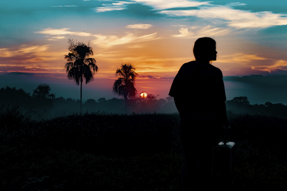 Silhouettenfotografie einer Person, die während der goldenen Stunde weit weg von Bäumen steht