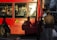 A red city bus features an advertisement for clean air initiatives in London. The bus's side windows reveal passengers inside, some using their phones. Shadows cast by pedestrians are visible on the bus. A person with a hat and carrying a bag is near the bus.