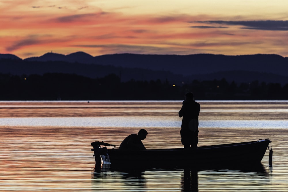 two person standing on boat on body of water during golden hour