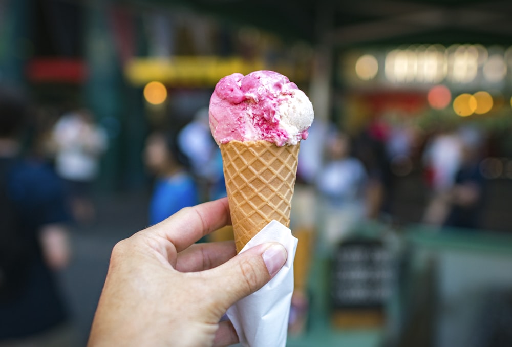 Persona sosteniendo helado blanco y rosado en la fotografía de foco superficial del cono