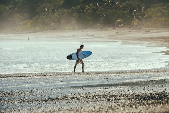 man in blue shirt holding white surfboard walking on beach during daytime in Playa Venao Panama