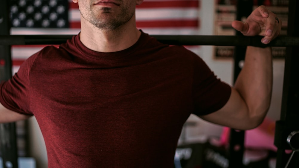 man wearing red crew-neck shirt carrying barbell