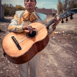 standing man holding brown sting musical guitar during daytime