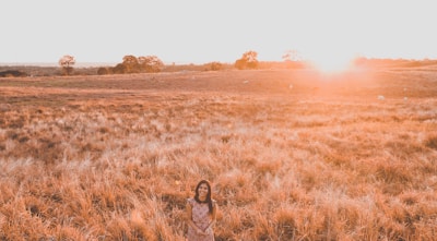 A joyful woman standing in a sunlit field, arms wide open, smiling confidently.