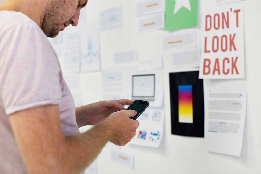 A man with a smartphone in front of document printouts and posters on a wall