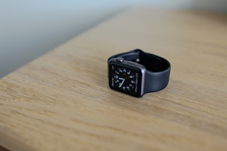 A sleek, modern smartwatch resting on a wooden desk next to a notebook and pen.