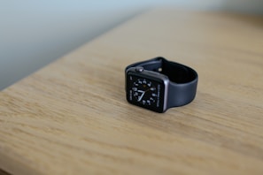 A sleek modern watch resting on a polished wooden surface with subtle reflections.