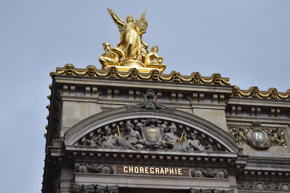 The image features an ornate architectural facade with elaborate carvings and a prominent gold statue at the top. The upper section includes detailed sculptures of figures and intricate designs, while the word 'CHOREGRAPHIE' is prominently displayed below.