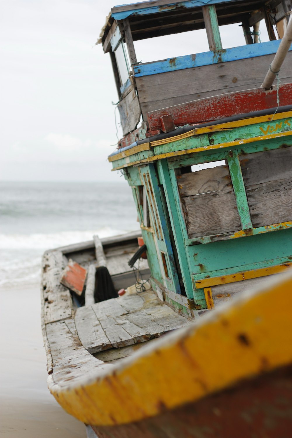 barco de madeira marrom e verde na areia marrom perto do mar durante o dia
