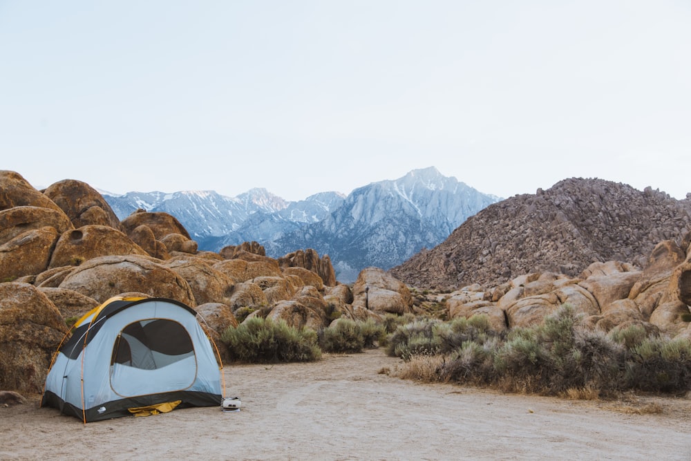 white and black dome tent setted up beside brown boulders overlooking mountain under white sky