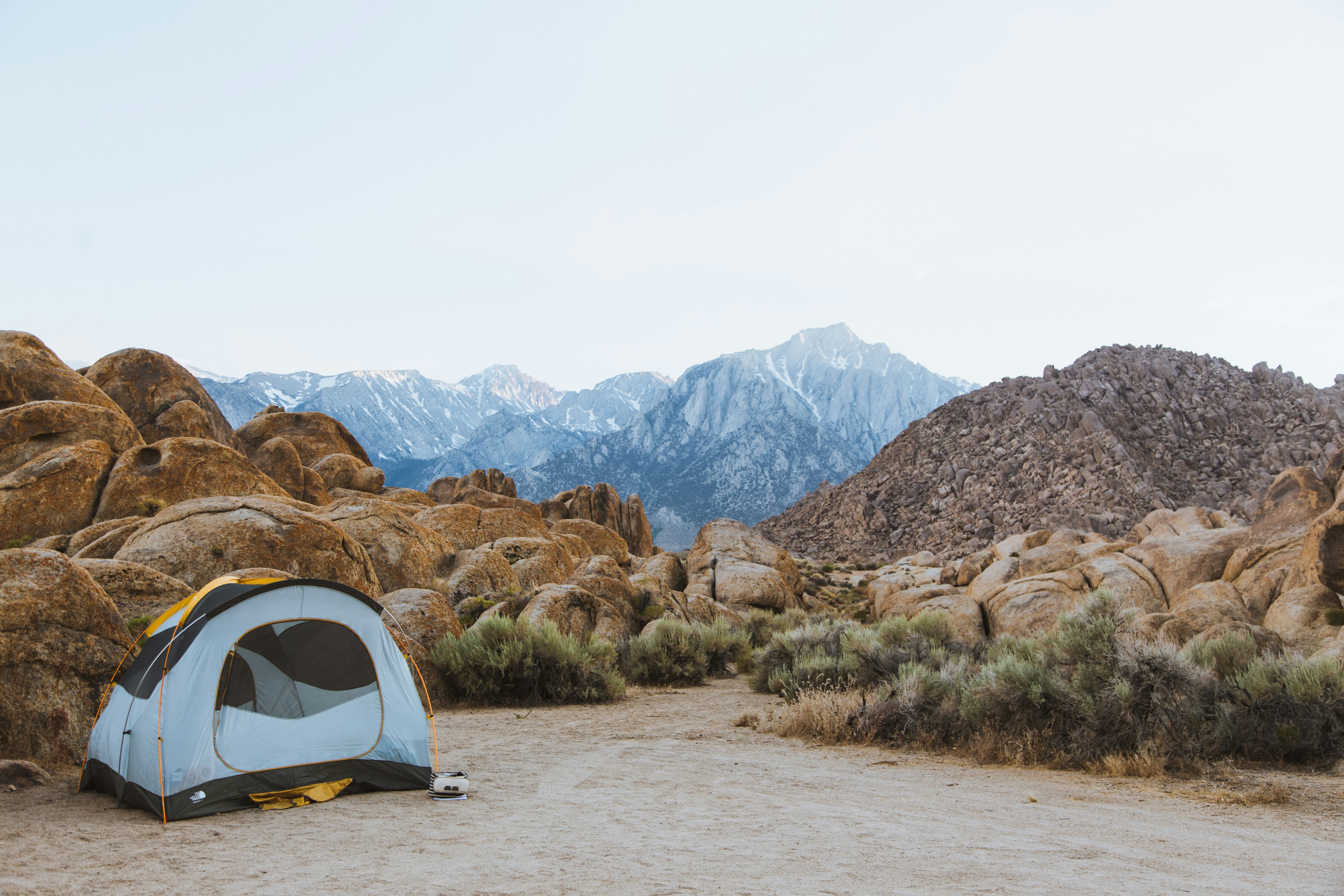 white and black dome tent setted up beside brown boulders overlooking mountain under white sky