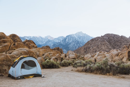 white and black dome tent setted up beside brown boulders overlooking mountain under white sky in Alabama Hills United States