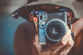person with brown bucket hat using black and grey Fujifilm Instax camera