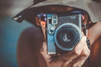 person with brown bucket hat using black and grey Fujifilm Instax camera
