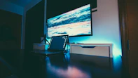 Minimalist workspace with navy blue walls, cyan lighting accents, and silver tech devices.