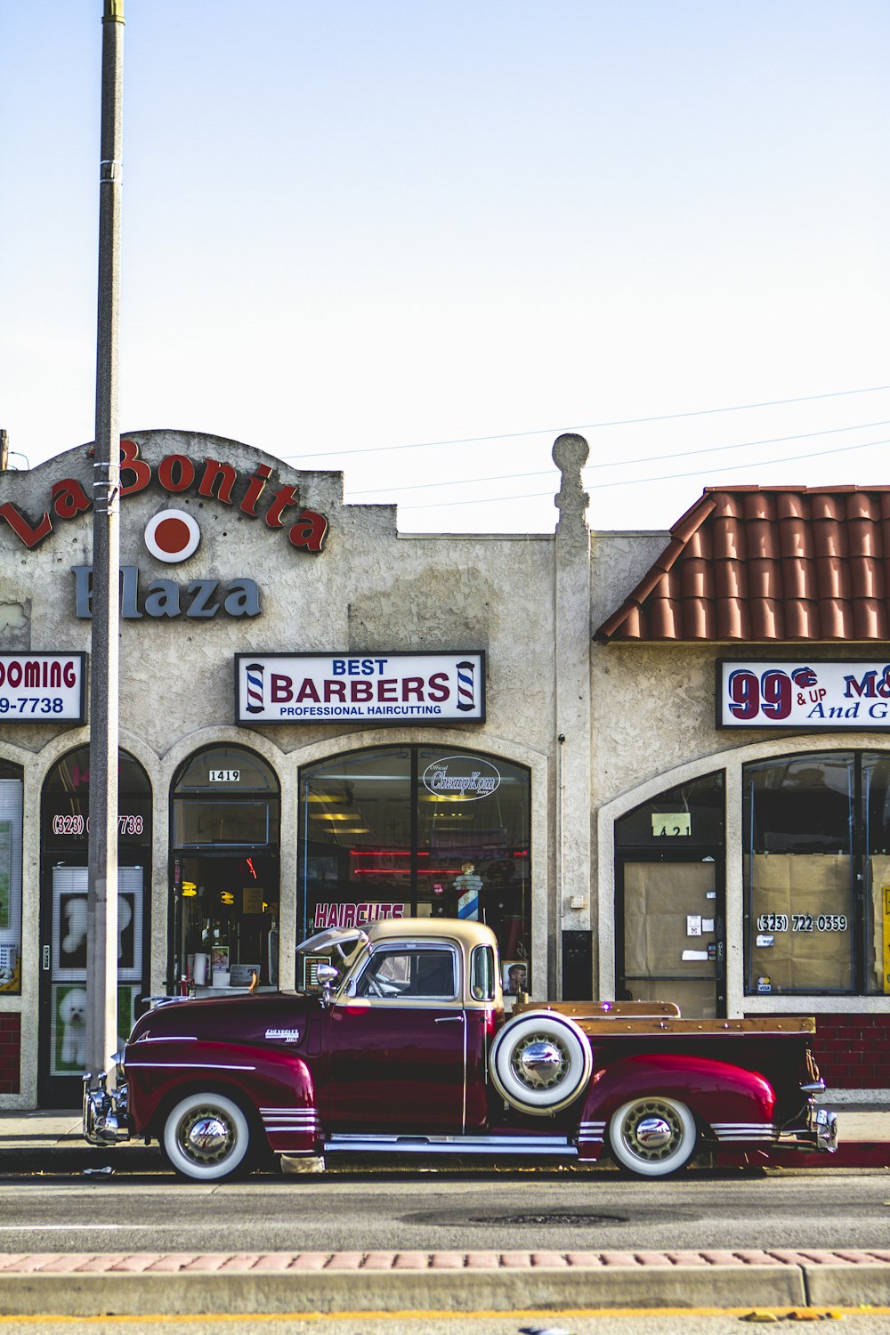 classic red coupe parked beside barber store facade