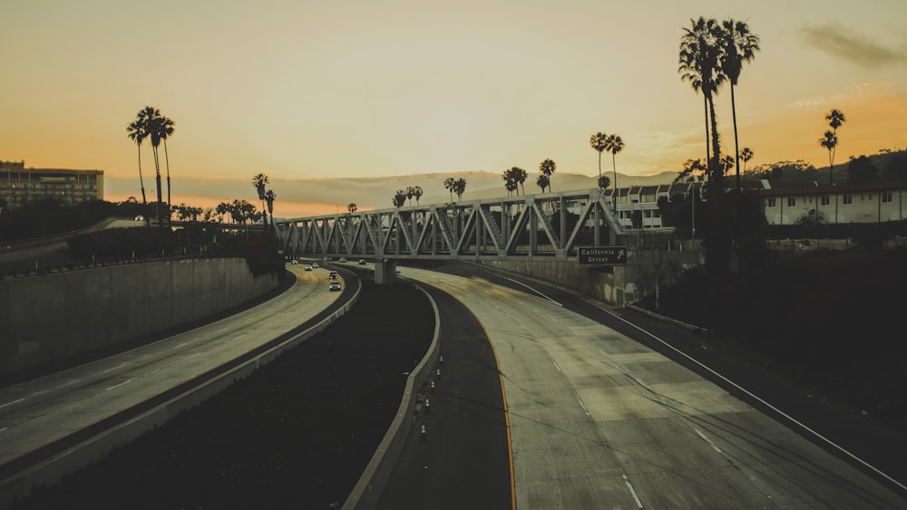 two gray concrete roads under gray truss bridge during sunset