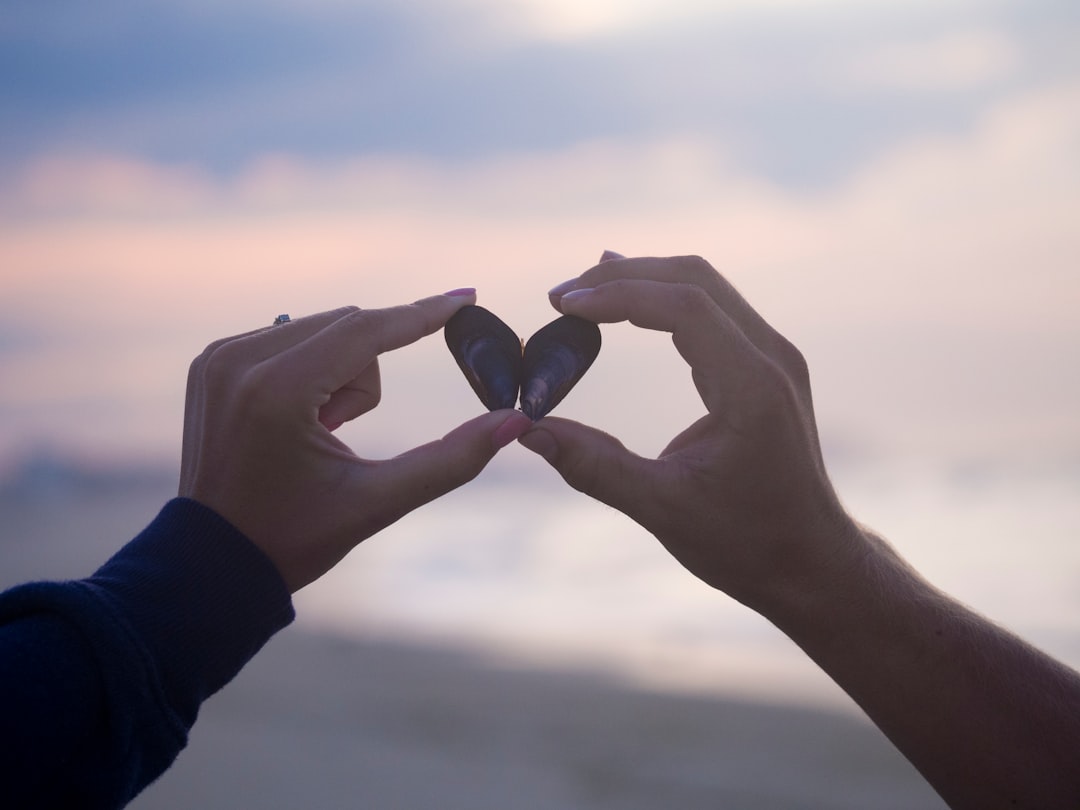 A couple holding two small shells next to each other to form a heart shape
