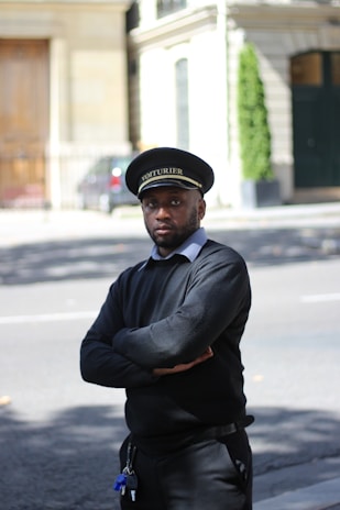A driver in uniform waving as they open the door for a customer at a busy city street.