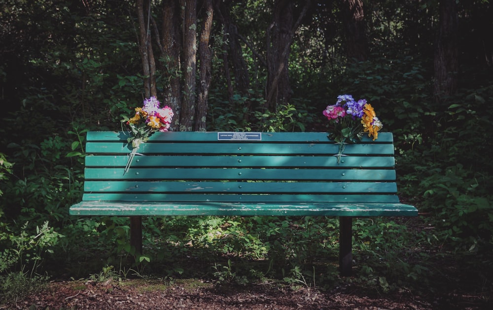 昼間の緑の木製ベンチと花