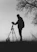 silhouette photo of man in front of DSLR camera with tripod under leafless tree