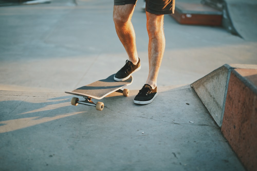 낮에 갈색 나무 스케이트보드 경사로 근처에서 검은색 스케이트보드를 밟고 있는 검은색 로우탑 운동화를 신은 사람