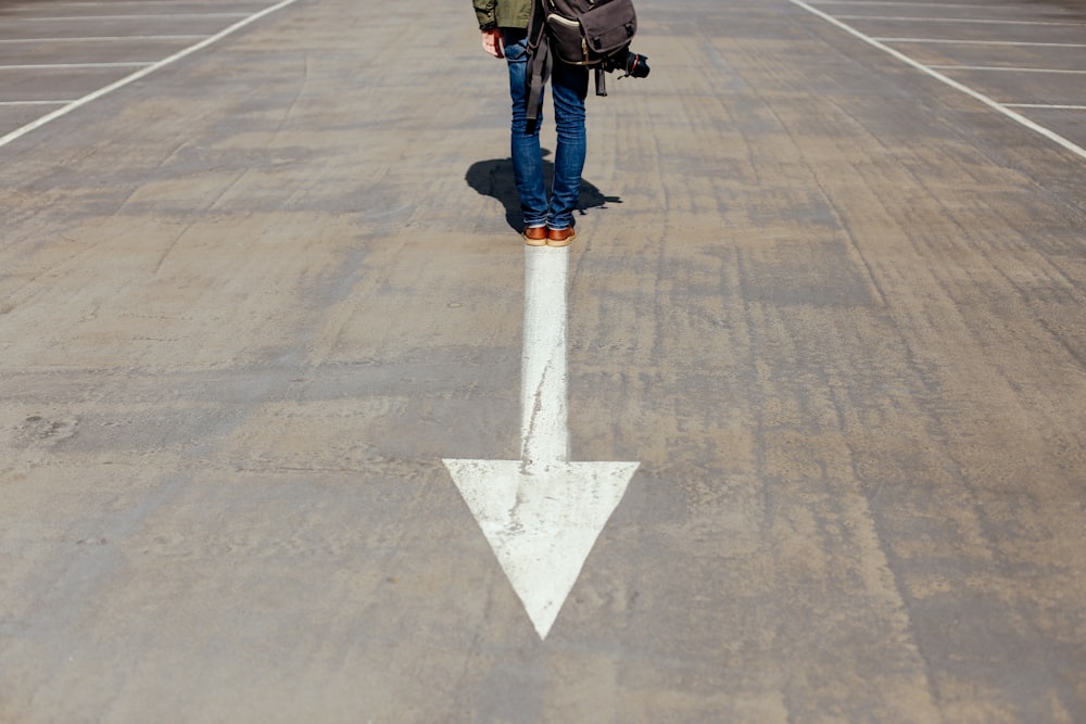 person standing on arrow sign on road