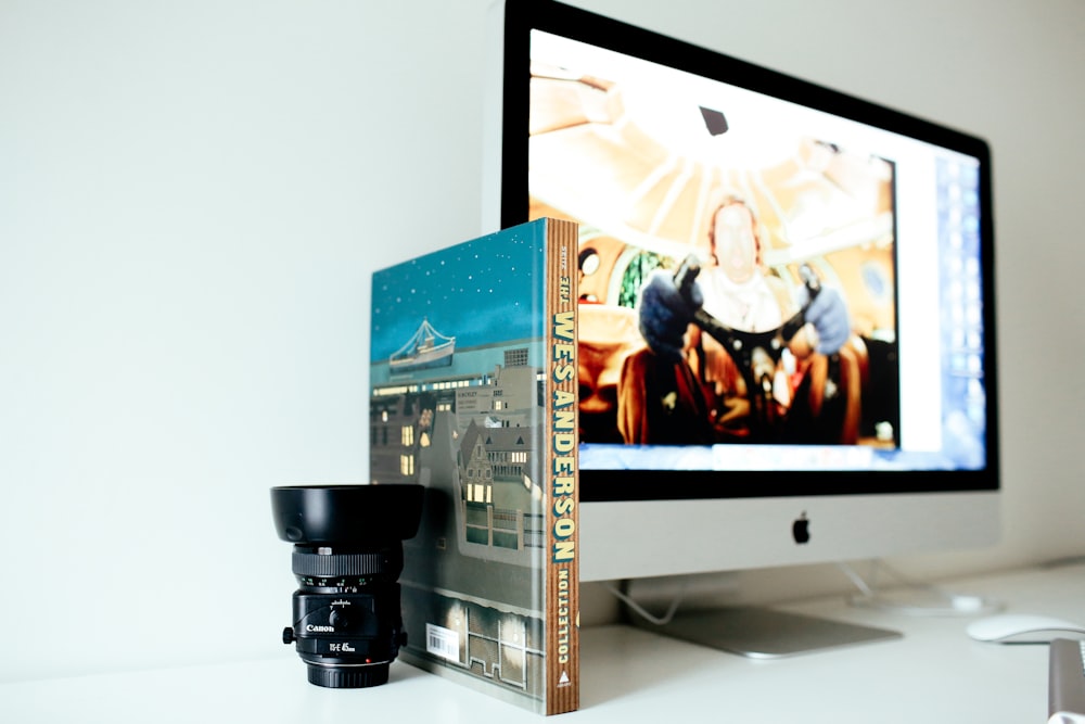 책 옆에 있는 검은색 카메라 렌즈의 선택적 초점 촬영과 iMac을 켭니다.