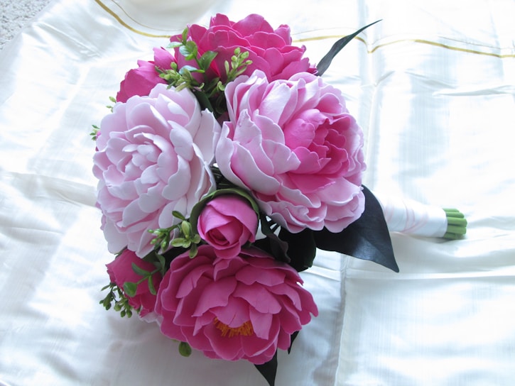 A delicate bouquet of soft pink peonies and white roses wrapped in elegant cream paper, resting on a marble table.