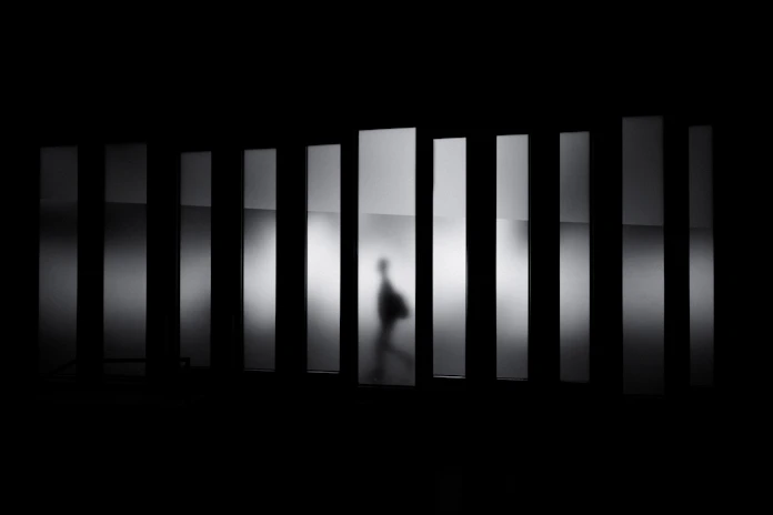 A person in silhouette walking behind a row of vertical frosted glass panels