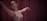 A dancer gracefully extends her arms while wearing a sleeveless sequined dress, performing against a backdrop of rich maroon curtains.