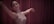 A dancer gracefully extends her arms while wearing a sleeveless sequined dress, performing against a backdrop of rich maroon curtains.