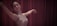 A dancer gracefully extends her arms while wearing a sleeveless sequined dress, performing against a backdrop of rich maroon curtains.