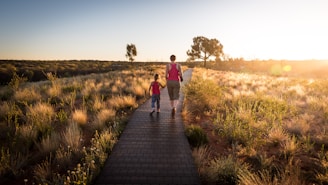 man and toddler with tank top walking on pathway between brown leaf plants during sunset