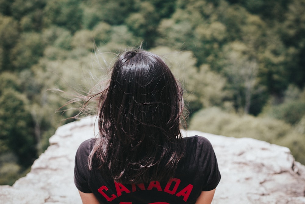 Mujer en la parte superior negra al lado en el acantilado de la montaña durante el día