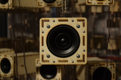 A close-up view of a wooden-cased speaker with visible screws, surrounded by similar speakers in the background, creating a repeating pattern.