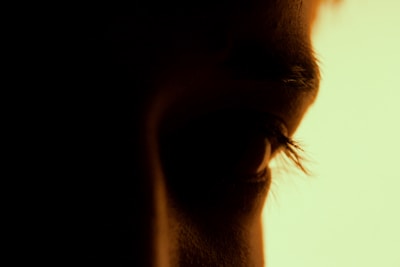 Close-up of a camera lens capturing a model’s expressive eyes in a shadowy setting.