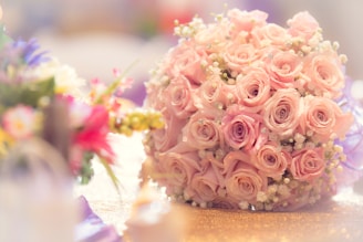 Elegant bouquet of soft pink roses wrapped in delicate white paper, set against a light airy background.