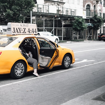 A friendly taxi driver opening the door of a clean, yellow taxi in front of a busy Tanger street.