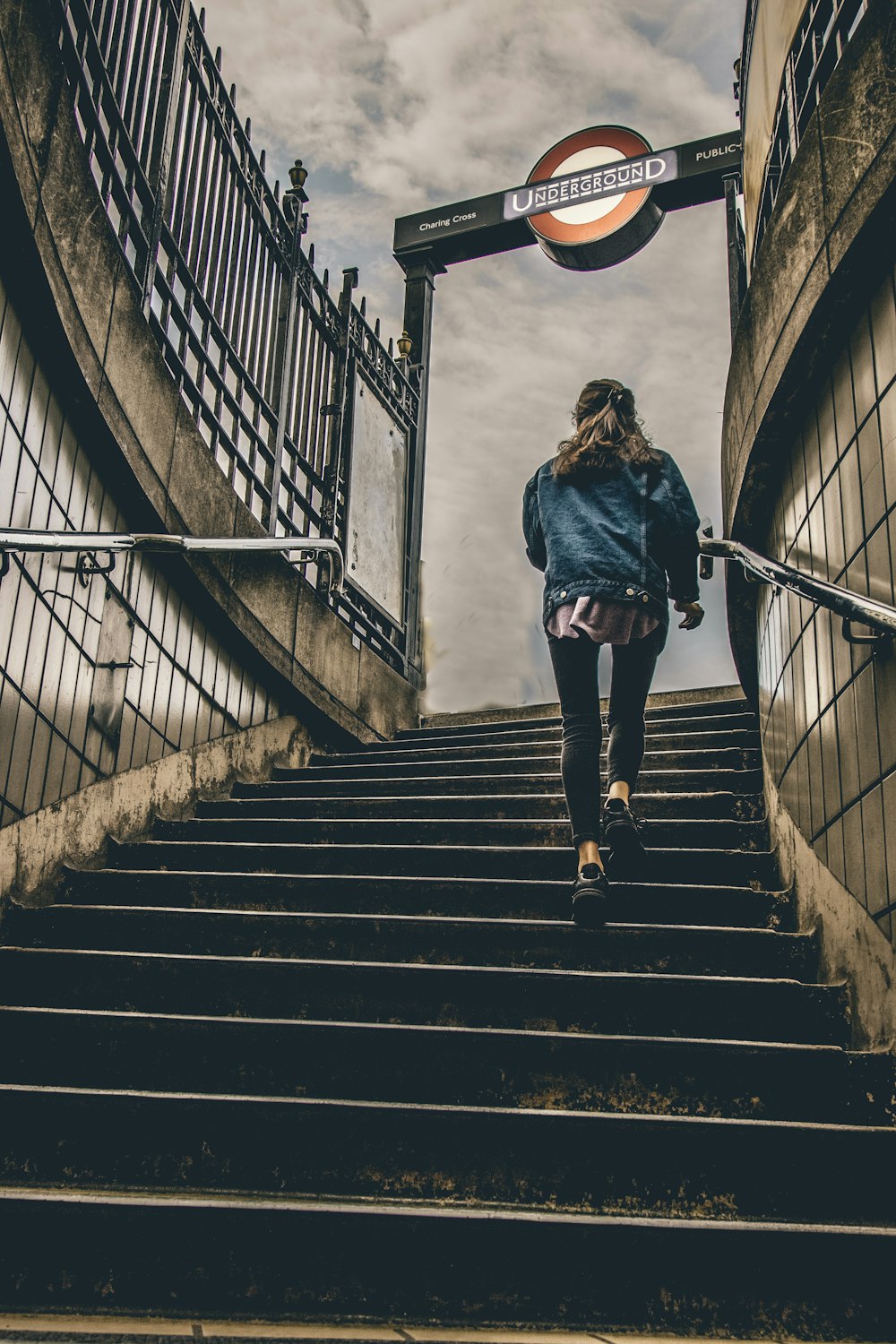 donna in giacca abbottonata in denim blu che cammina su scale di cemento durante il giorno