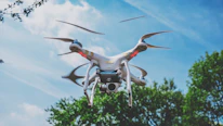 A red drone mid-flight against a soft beige sky, with trees faintly visible in the background.