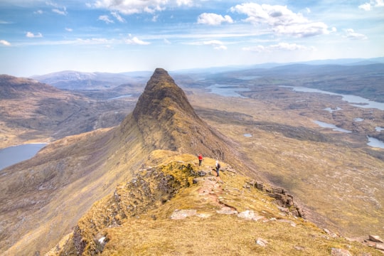 2 person standing on hill under white cloudy sky in Suilven United Kingdom