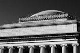 A grand architectural structure with classical columns and ornate detailing, featuring inscriptions on the facade, including references to a college founded in New York.