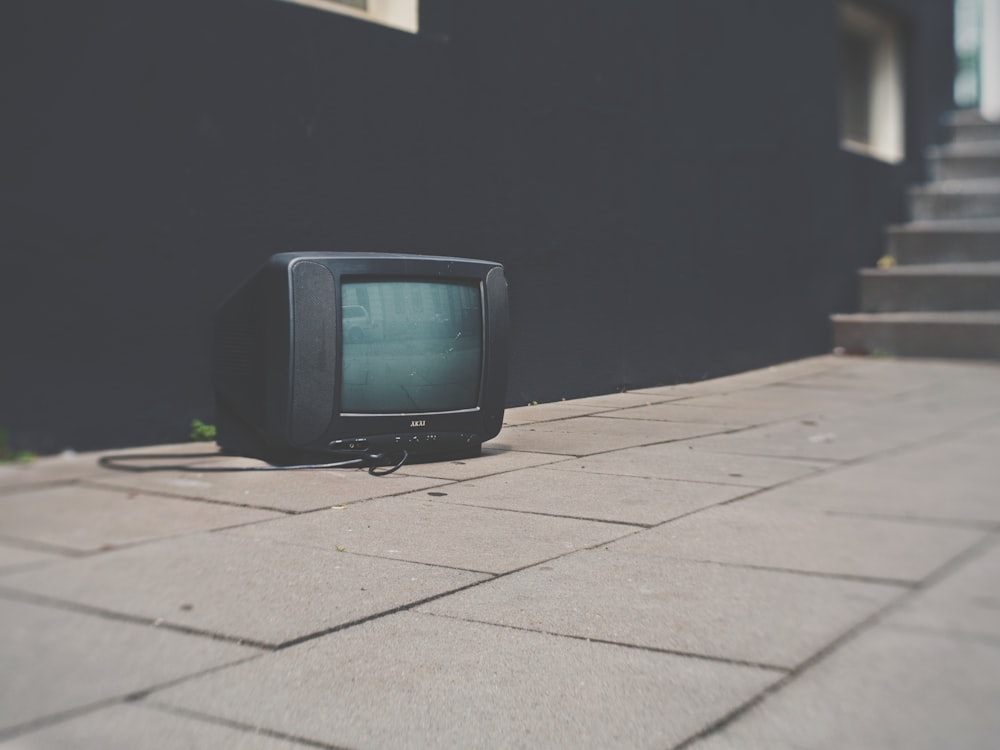 Television with cord sitting on sidewalk outside of black building near stairs
