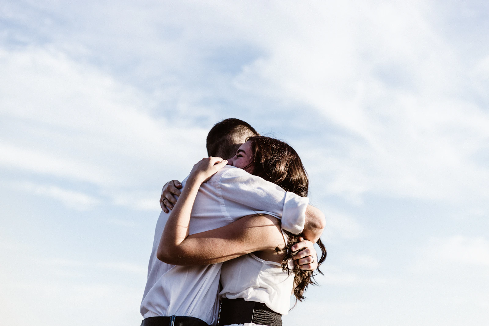 Two people sharing a warm, comforting hug outdoors under a bright sky