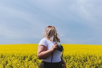 woman holding DSLR camera standing in front of yellow flower field