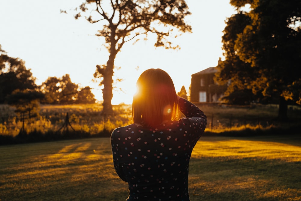 woman wearing black long-sleeved top standing on lawn during sunset