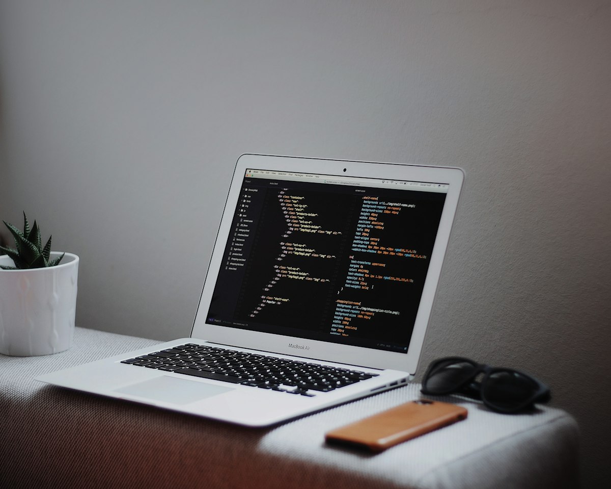 Laptop showing code on a desk by a plant